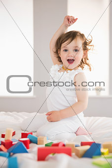 Cute happy girl playing with building blocks on bed
