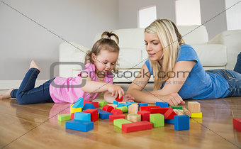 Mother and daughter playing with building blocks on floor