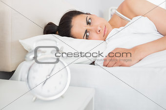 Beautiful young woman looking at alarm clock