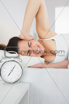 Sleepy woman covering ear with hand in bed