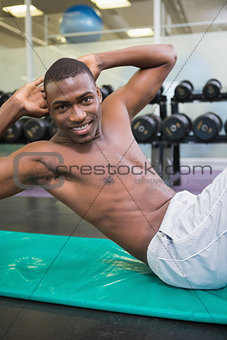 Portrait of shirtless man doing abdominal crunches in gym