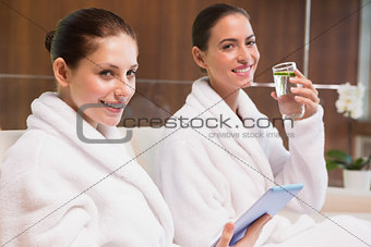 Women in bathrobes drinking water and text messaging