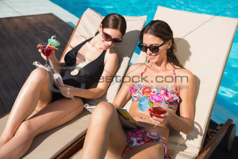 Women with drinks reading books by swimming pool
