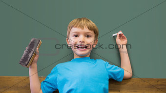 Happy pupil holding chalk and duster in classroom