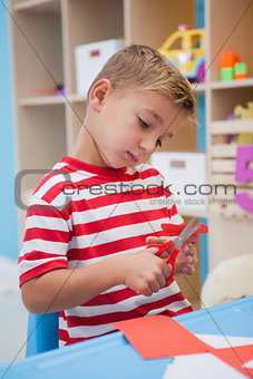 Cute little boy cutting paper shapes in classroom