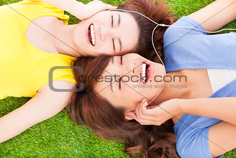 two pretty young woman lying on grassland and listening music 
