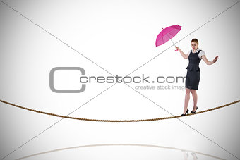 Composite image of pretty redhead businesswoman holding umbrella on tightrope