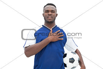 Football player in blue standing with the ball listening to anthem