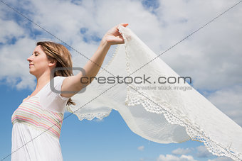 Woman holding out scarf against blue sky and clouds
