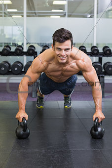 Muscular man doing push ups with kettle bells in gym