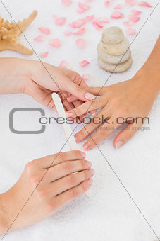Beautician filing female client's nails at spa beauty salon