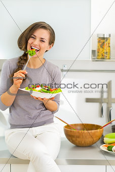 Happy young woman eating greek salad in modern kitchen