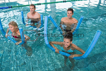 Happy fitness class doing aqua aerobics with foam rollers