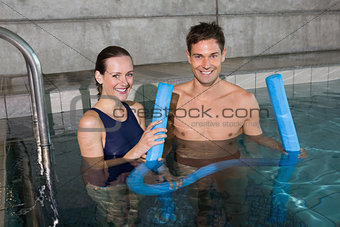 Happy couple holding foam rollers smiling at camera