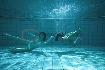 Pretty friends looking at camera underwater in bikinis