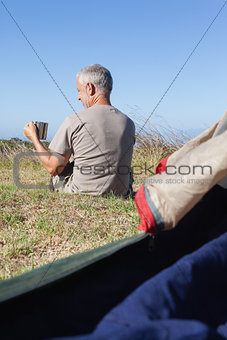 Happy camper sitting outside his tent holding mug