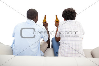Two sports fans sitting on the couch with beers