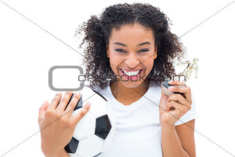 Pretty football player in white holding winners figurine and ball