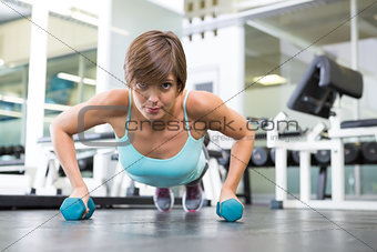 Fit brunette in plank position with dumbbells