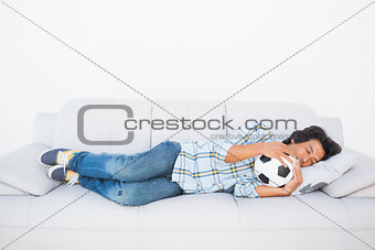 Football fan sleeping on couch hugging ball