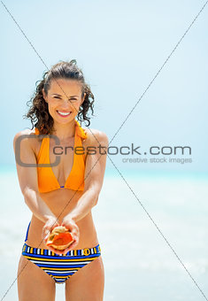 Portrait of happy young woman showing shell on beach
