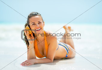 Happy young woman laying on sea shore and listening sound of sea