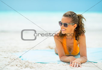 Smiling young woman in sunglasses laying on sea coast looking on