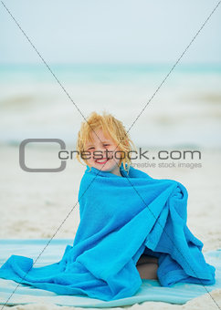 Smiling baby girl wraped in towel sitting on beach