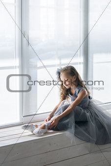Little ballerina in gray dress puts on ballet shoes pointe front