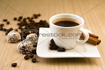 Cup of coffee with beans and truffles over wooden background