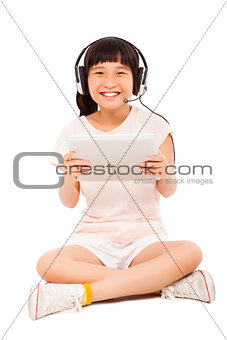 sitting little girl holding a tablet with earphone 