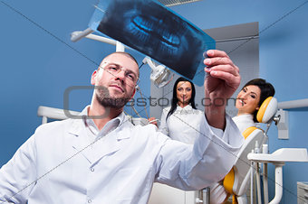 Dentist with x-ray and smiling patient and assistant in the background