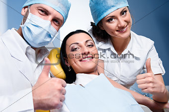 Friendly male dentist with assistant and smiling patient showing thumb up