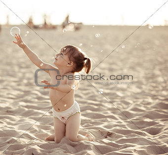 Adorable baby girl playing with soap bubbles on the beach
