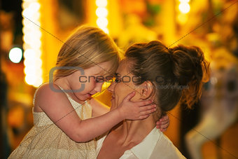 Portrait of mother and baby girl hugging in front of carousel
