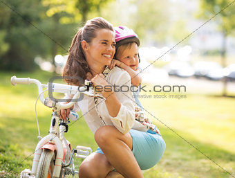 Portrait of baby girl hugging mother near bicycle in park