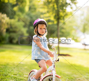 Portrait of displeased baby girl with bicycle in park