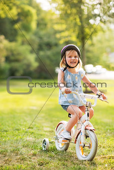Portrait of happy baby girl riding bicycle outdoors in park