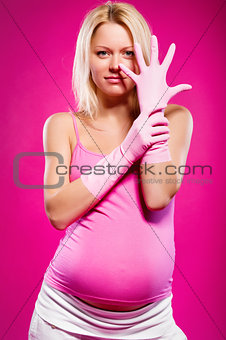 Pregnant attractive woman wearing rubber gloves posing over pink