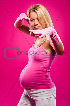 Pregnant attractive woman wearing rubber gloves posing over pink