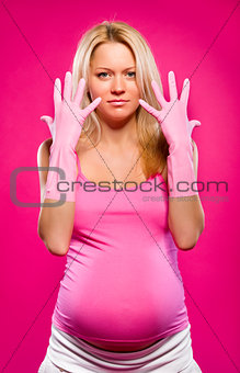 Pregnant attractive woman wearing rubber gloves posing over pink