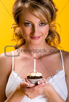 Beautiful young woman with birthday cake over yellow background 