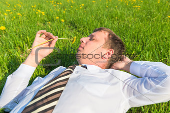 businessman lying on the grass and sniffs dandelion