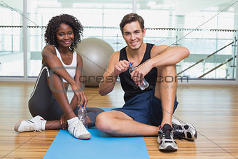 Personal trainer and client smiling at camera on exercise mat