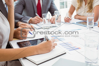 Mid section of executives writing notes in board room meeting