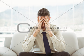 Worried businessman with head in hands sitting on couch