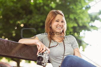 Smiling redhead sitting on bench holding her camera