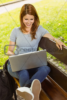 Happy girl sitting on bench using laptop