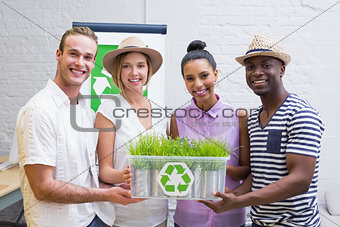 Creative business team holding plant with recycling symbol