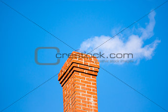 Brick chimney releasing smoke on sky.